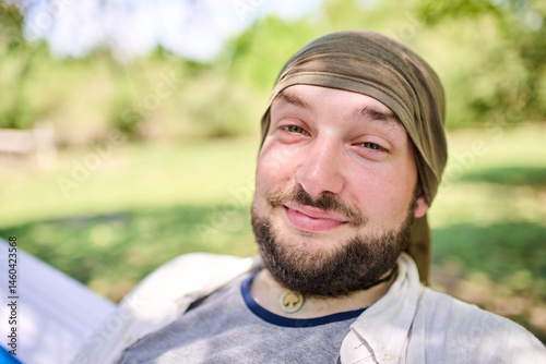 Portrait of a young hispanic man smiling and looking at the camera as he sits relaxed in a hammock, relaxing outdoors. His expression is that of a friendly and cheerful person.