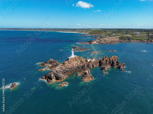 Scenic aerial drone view of La Corbiere lighthouse on a rocky island surrounded by the blue sea. Jersey, Channel Islands