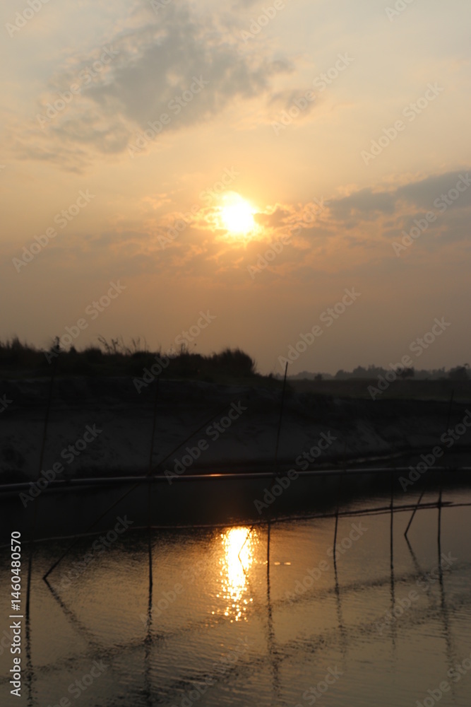 Sunrise Over Calm Water Reflecting Light With Distant Land And Clouds Silhouette