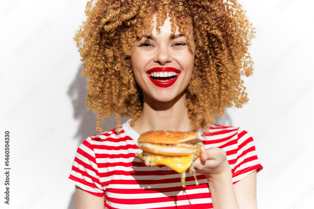 Happy woman with curly hair enjoying a delicious burger, wearing a striped shirt and bright red lipstick, against a clean white background