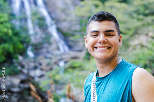 Portrait of a male explorer smiling at the camera, with a large waterfall in the background, showcasing his adventurous freelancer side.
