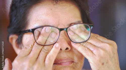 Elderly person rubbing eyes behind eyeglasses showing tiredness and eye strain close up with hands on lenses and signs of fatigue