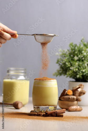 dusting cinnamon powder into a glass of turmeric latte