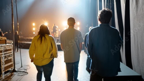 This captivating image shows silhouettes of three individuals walking towards a stage filled with lights, representing anticipation and excitement before a live performance.