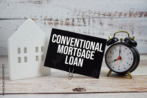 Conventional Mortgage Loan on paper card with alarm clock and white house model on wooden background