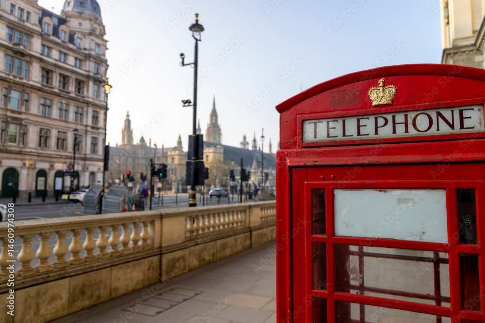 Fototapeta premium A striking, vibrant red telephone box stands out prominently on a busy London street, with several iconic landmarks visible in the background, showcasing the unique charm and beauty of the city