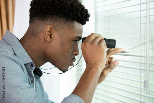 suspicious man looking through window blinds with binoculars