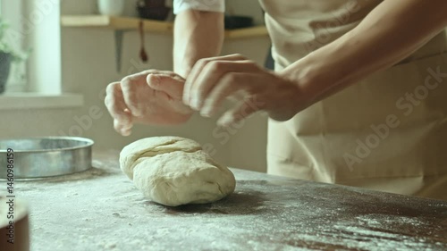 A baker in an apron kneads the dough with his hands and sprinkles it with flour to bake delicious homemade bread.