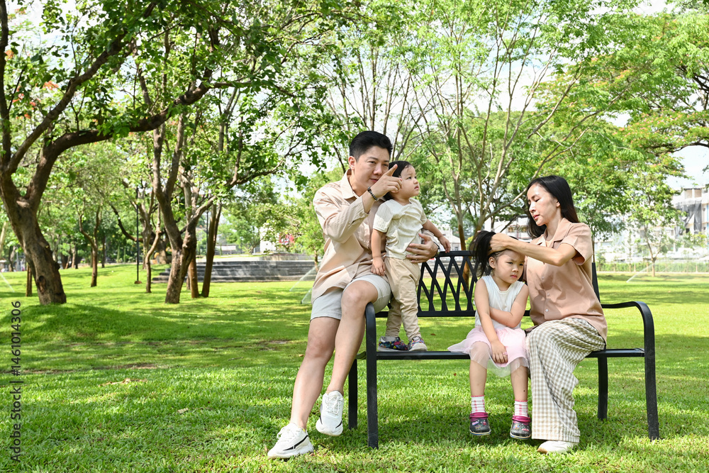 A family of four sits on a park bench, enjoying each other's company.
