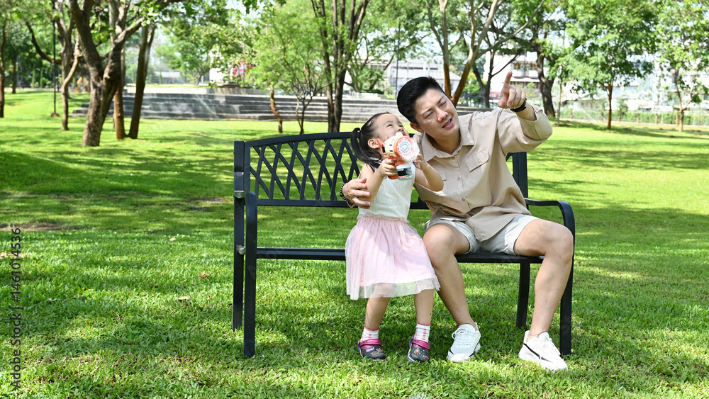 A man and a little girl are sitting on a park bench, Scene is warm and friendly, as the man and the girl seem to be enjoying each other's company.