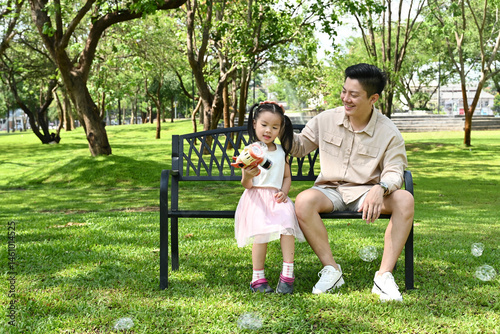 Fotografie A man and a little girl are sitting on a park bench, Scene is warm and friendly, as the man and the girl seem to be enjoying each other's company