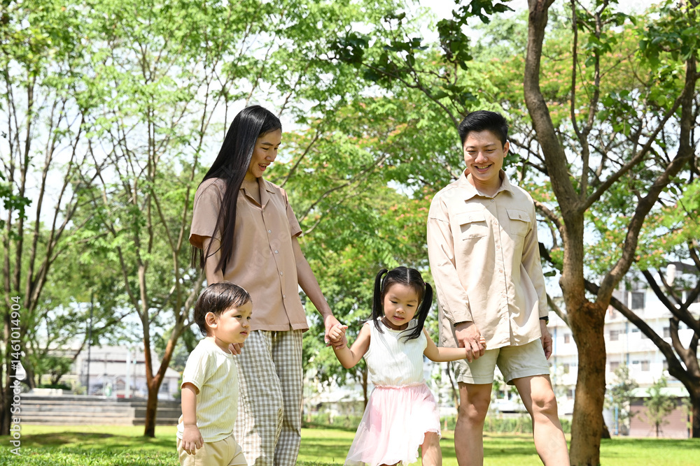 A family of four is walking in a park, the family appears to be happy and enjoying their time together.