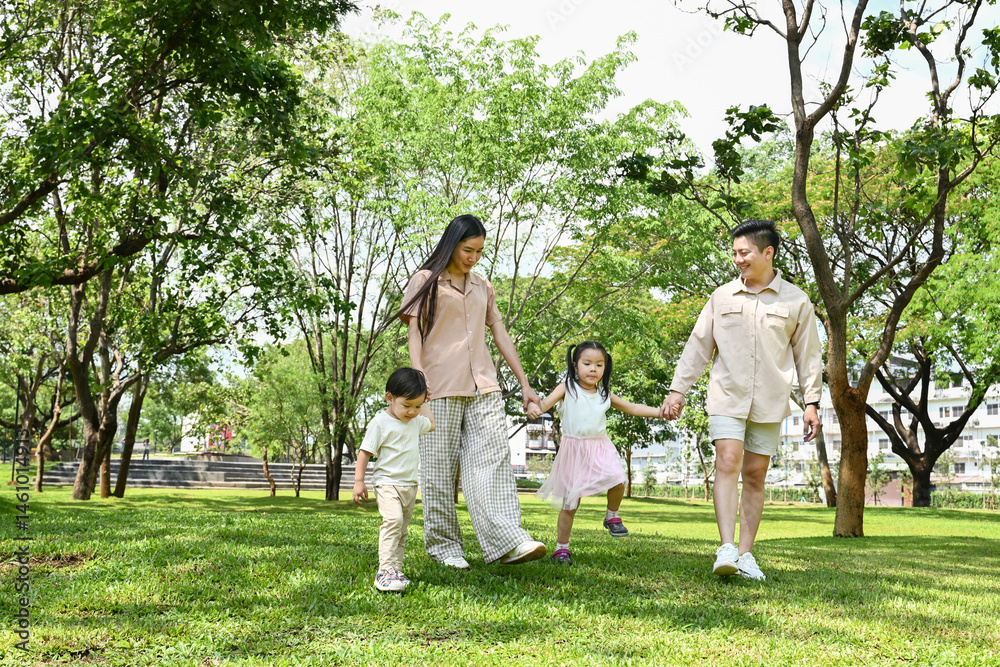 A family of four is walking in a park, the family appears to be happy and enjoying their time together.