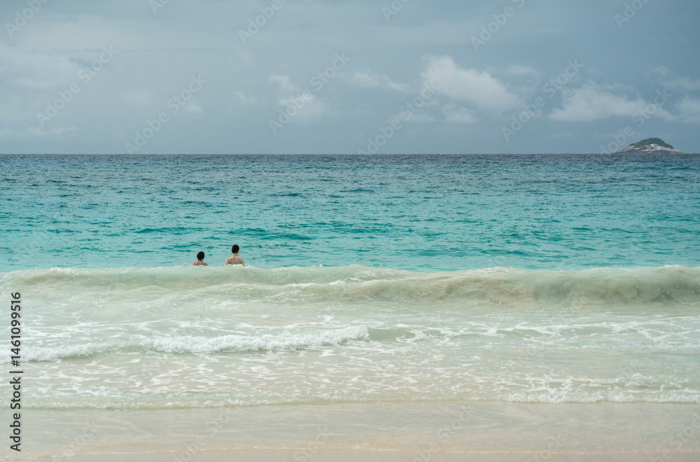 Tropical turquoise wave rolling to sandy beach in Seychelles, with foamy surf, calm horizon