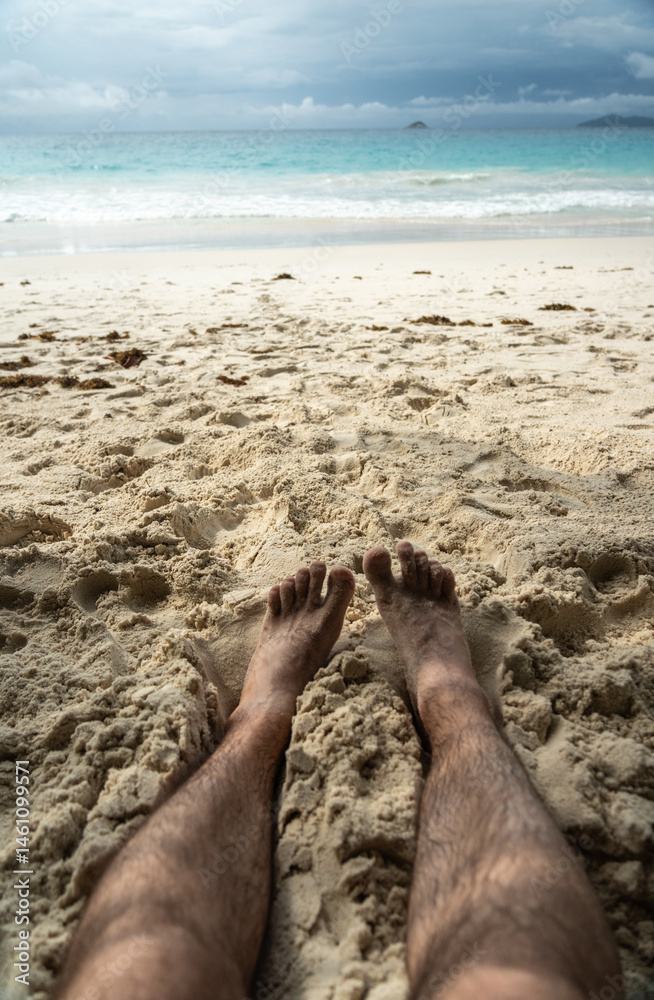 Bare feet resting in warm sand on tropical beach, symbolizing summer relaxation, freedom