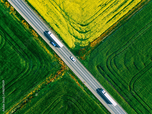 Aerial view of white trucks and cars driving on asphalt road along the green and yellow fields in Finland. Cargo delivery logistic concept