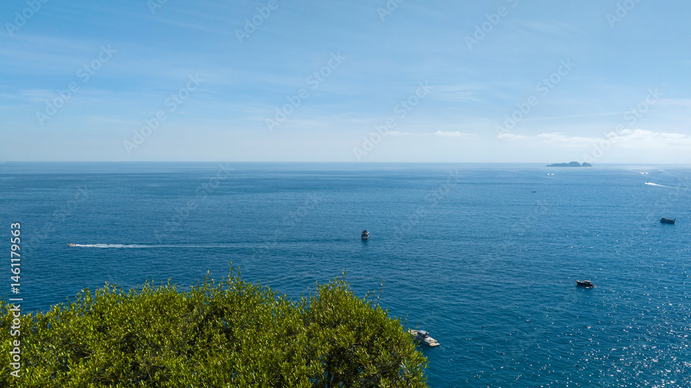 Panorama of the sea on the Amalfi coast. In the foreground the green foliage of a tree. In the background the sea touches the sky on the horizon.
