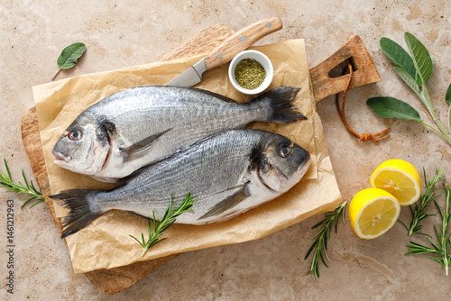 Fresh raw sea bream fish or dorado fish with lemon and herbs, top view