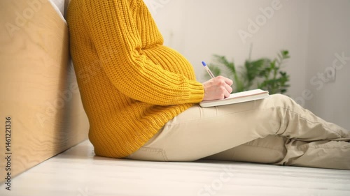 Expecting mother writing essential items list for maternity hospital in cozy home setting. Organized preparation for upcoming delivery and baby arrival.