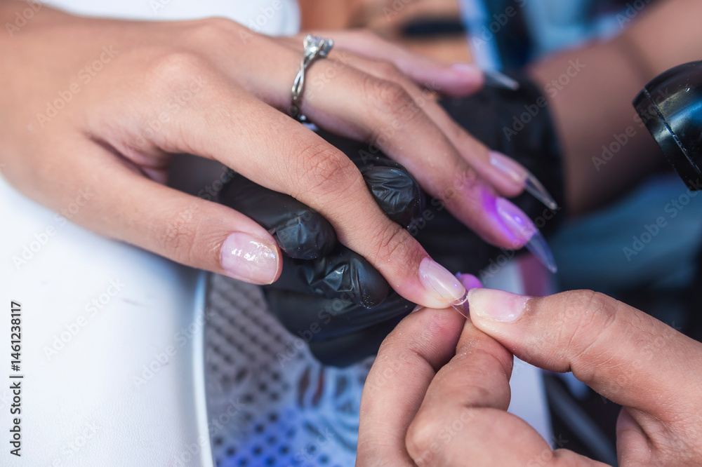 Fototapeta premium Close-up of a beauty technician pressing a soft gel tip onto the nail surface using adhesive during a manicure or nail art session in a salon environment.