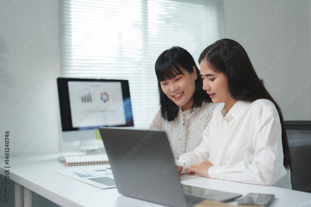 Two asian businesswomen collaborating in a modern office, working together on a laptop while analyzing financial charts and discussing strategies for success and growth Two asian businesswomen collaborating in a modern office, working together on a laptop while analyzing financial charts and discussing strategies for success and growth