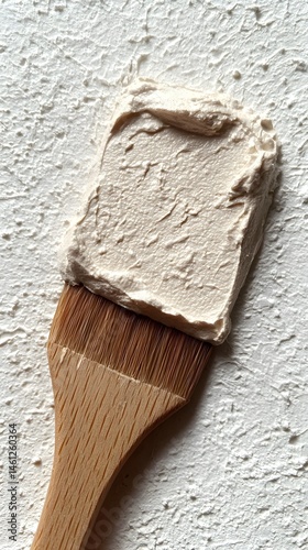 Beige Cream Swatch on Wooden Spatula Against White Textured Background
