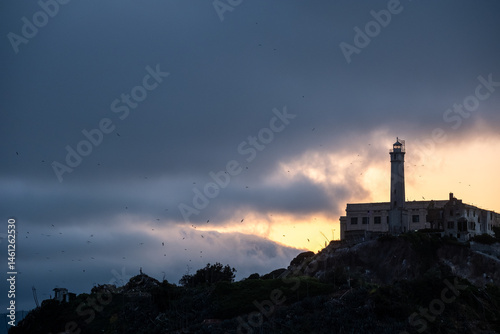 Final light outlines the silhouette of Alcatraz lighthouse and compound against heavy dusk clouds and fading sky – San Francisco, CA on May 11, 2019