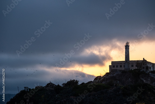 Tower of Alcatraz standing alone against a cloud-draped horizon glowing with golden sunset light and dark water in foreground – San Francisco, CA on May 11, 2019