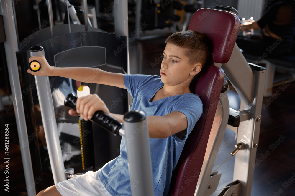 Teen boy doing sports exercise at machine for chest muscles pumping