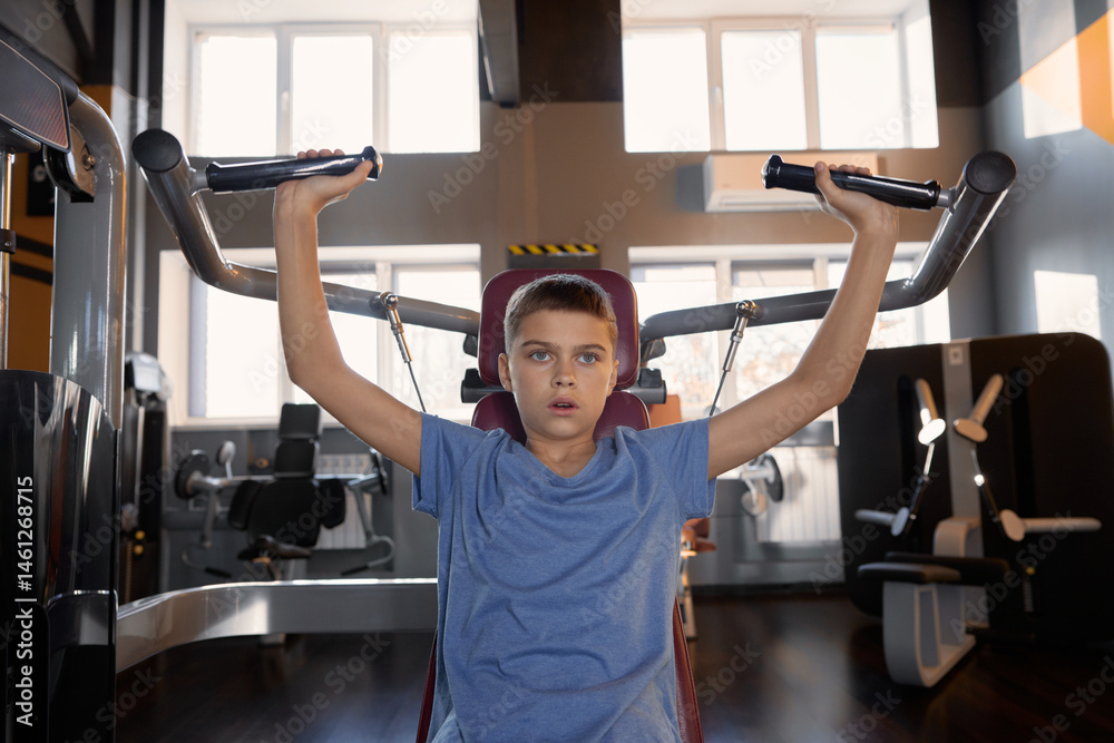 Teenager boy doing sports exercise at machine for chest muscles pumping