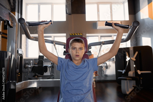 Obraz na płótnie Teenager boy doing sports exercise at machine for chest muscles pumping w salonie