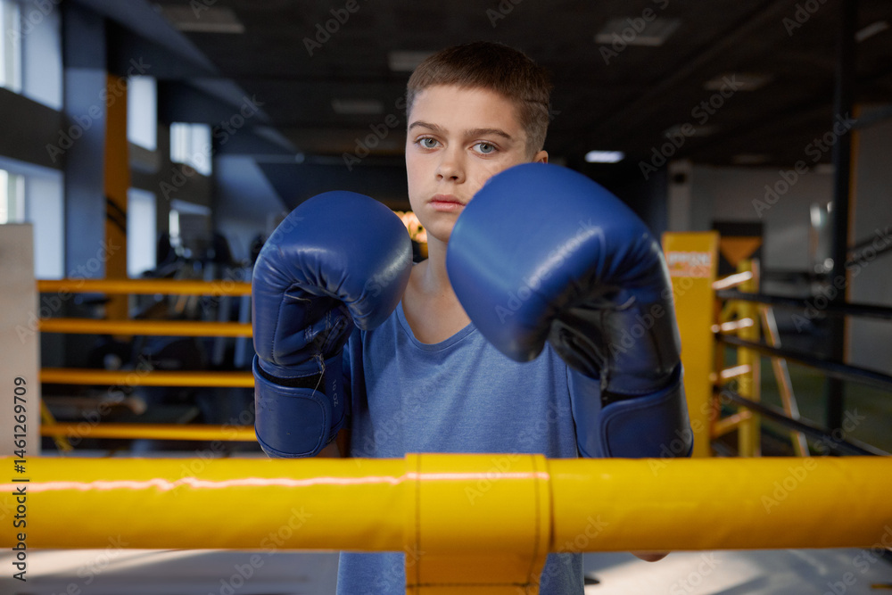 Teenage boy boxer wearing gloves inside boxing ring posing for camera