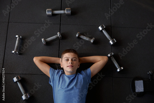 Obraz na płótnie Overhead portrait view on boy lying on gym floor surrounded by dumbbells w salonie