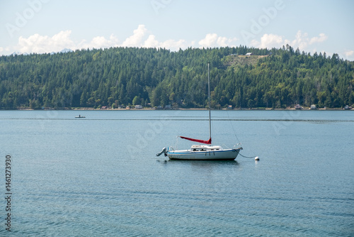 A single sailboat rests off the coast near Seattle with forested shoreline behind and soft clouds above, captured May 31, 2019, in Seattle, WA, USA