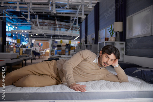 Obraz na płótnie Man relaxes on a modern mattress in a stylish showroom, showcasing ultimate comfort and tranquility w salonie
