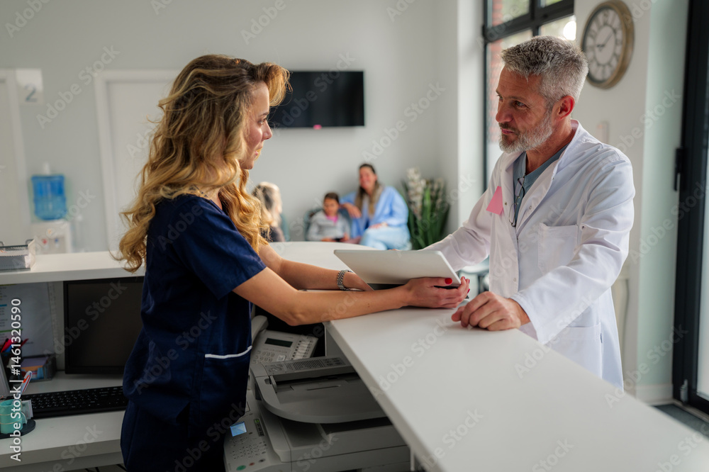 Obraz premium Doctor and a nurse are discussing patient information using a tablet in a hospital or clinic reception area, with a family waiting in the background