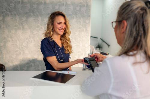 Smiling nurse accepting contactless payment from a patient at the reception desk of a modern medical clinic, highlighting convenient and efficient healthcare transactions