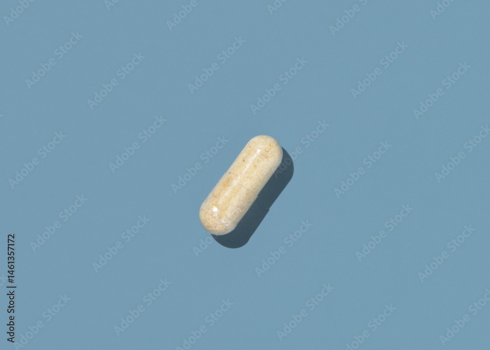 Beige Medical capsule on blue top view, hard shadows. Taking dietary supplements