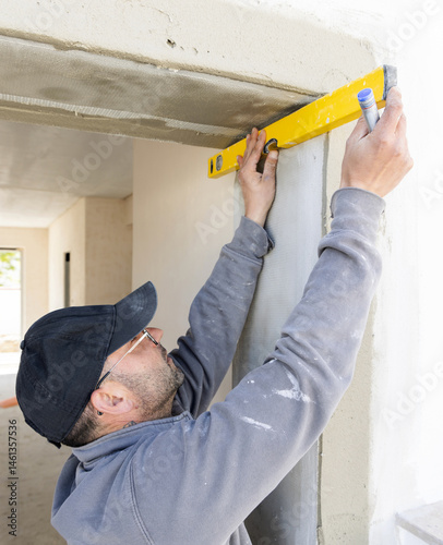 Obraz na płótnie Craftsman in grey work clothing uses a yellow level to control a house wall. Construction process w salonie