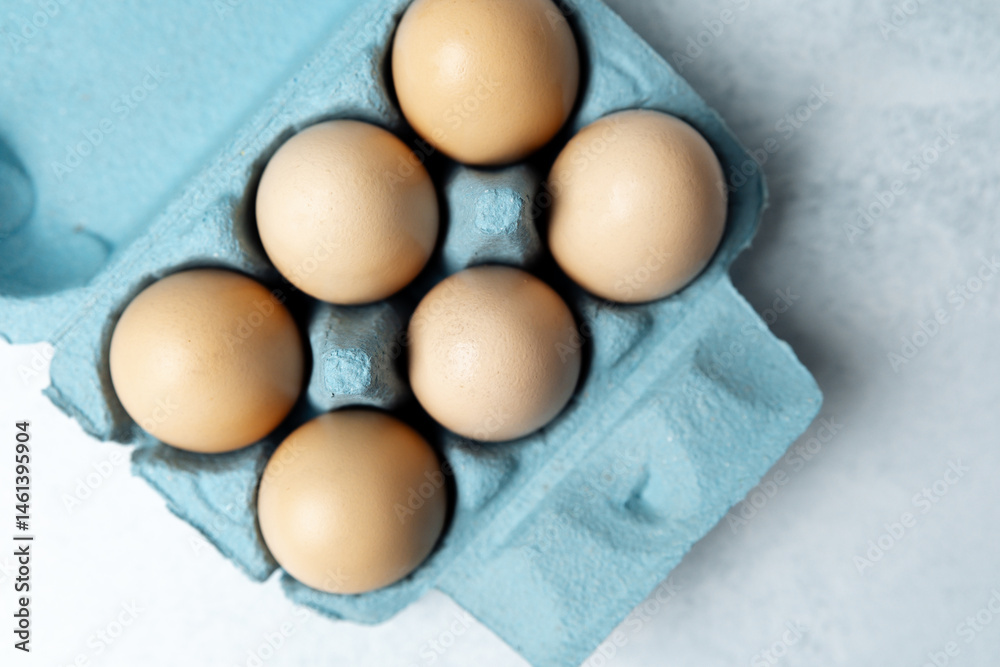 Brown chicken eggs in a blue carton box on light blue background, top view