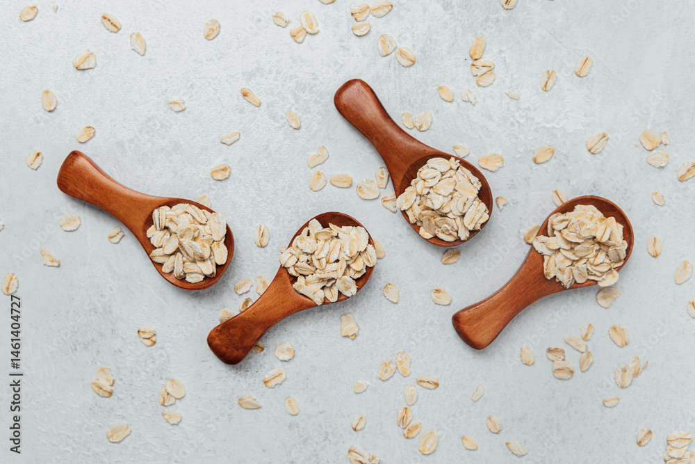 Various wooden spoons filled with oats on a light textured surface