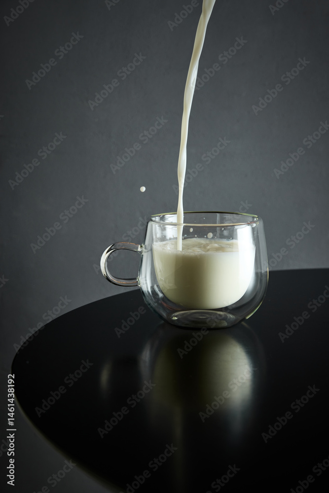 Milk pours smoothly into glass cup creating elegant ripple on glossy black table surface. Concept of drink, organic food, aesthetics, advertisement