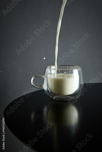Obraz na płótnie Milk pours smoothly into glass cup creating elegant ripple on glossy black table surface. Concept of drink, organic food, aesthetics, advertisement w salonie