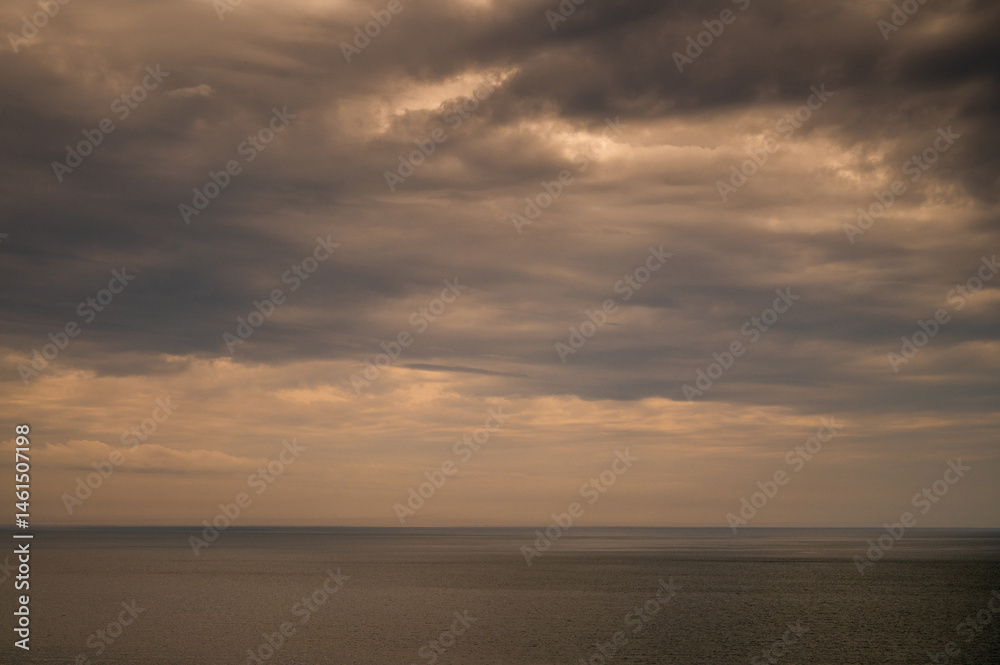 Sun between dark storm clouds over ocean. Dramatic seascape. Clouds and rain flurry over sea.