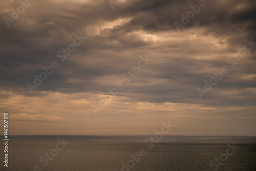 Obraz na płótnie Sun between dark storm clouds over ocean. Dramatic seascape. Clouds and rain flurry over sea. w salonie
