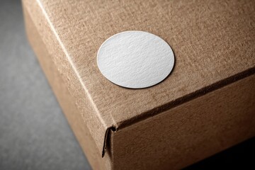 Close up of a blank white round sticker on a brown cardboard box, presenting a clean and simple design with natural textures, perfect for branding and packaging mockups.