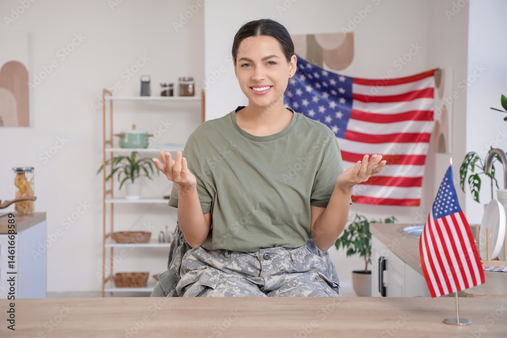 Fototapeta premium Female soldier with USA flag video chatting at table in kitchen
