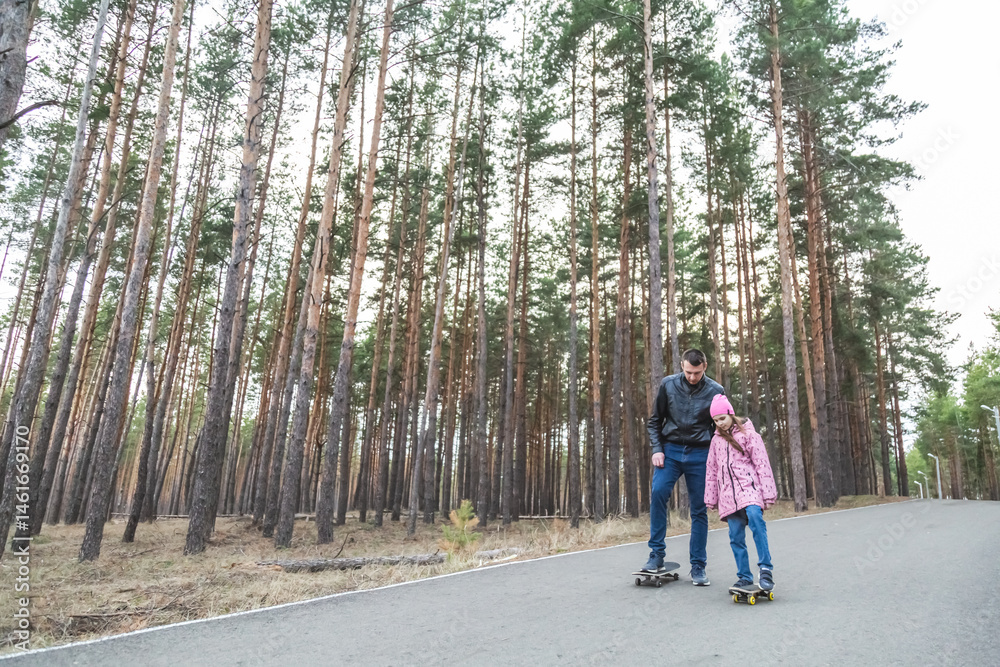 Father and his little daughter ride skateboards in the forest Father and his little daughter ride skateboards in the forest
