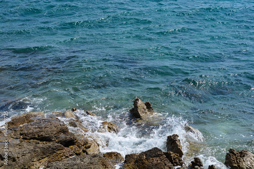 Obraz na płótnie Dark blue sea waves crash against rugged, dark rocks along the shore, creating white foamy splashes under natural light w salonie
