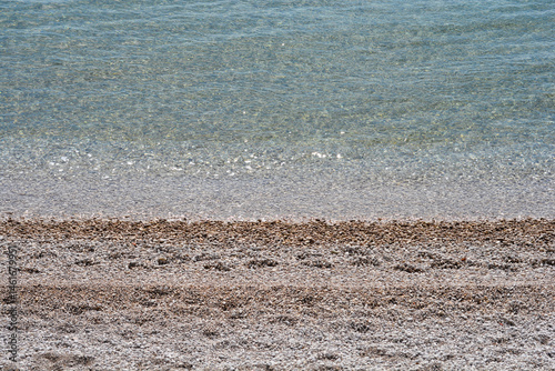 Obraz na płótnie Clear turquoise sea gently washes over a pebble beach under a bright sky w salonie